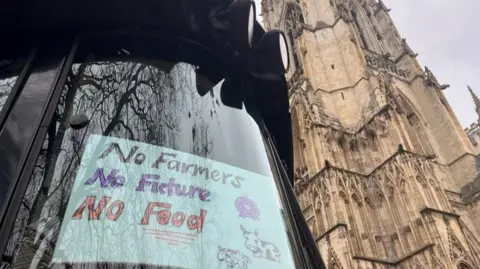 Julia Lewis/BBC Tractor with a sign in its window next to York Minster