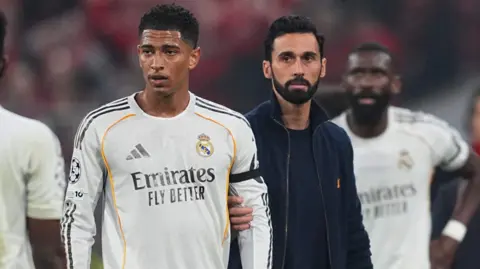 Real Madrid's Jude Bellingham is held back by manager Alvaro Arbeloa after they are knocked out of the Champions League by Bayern Munich