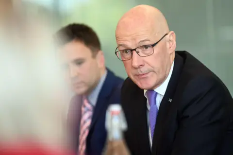 PA Media John Swinney sits at a table with worker and union representatives