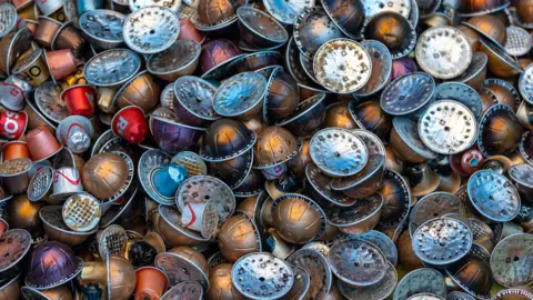 Barbara Evripidou Used coffee pods in various colours and sizes. They have coffee grounds on them and have holes punctured into their tops.