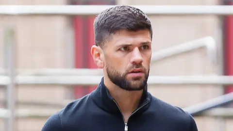 Joe Cordina, a man with brown hair and a brown beard. He's wearing a navy quarter-zip. 