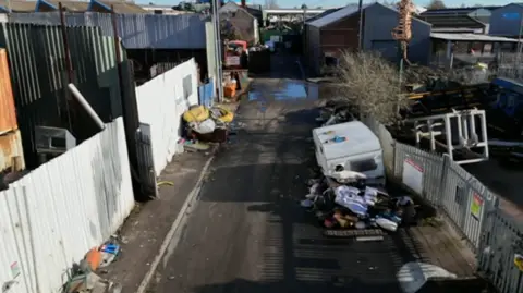 An aerial image of a road that goes from bottom to nearly the top of the photo in the middle. Rubbish in on a pavement on the left and on the road on the right.