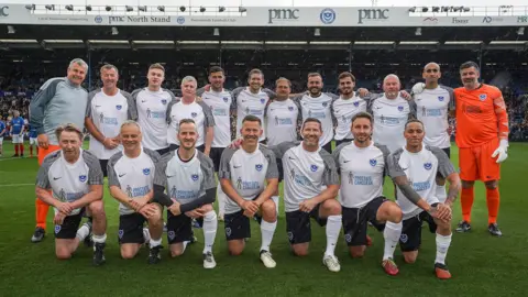 Jason Brown Photography A team of nineteen footballers dressed in matching kits, arranged in two rows and smiling at the camera. They're in a stadium and there's raked seating behind them.