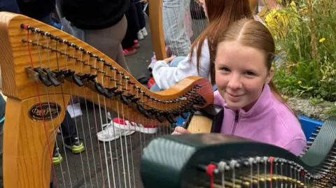 A young girl smiles as she cradles her harp