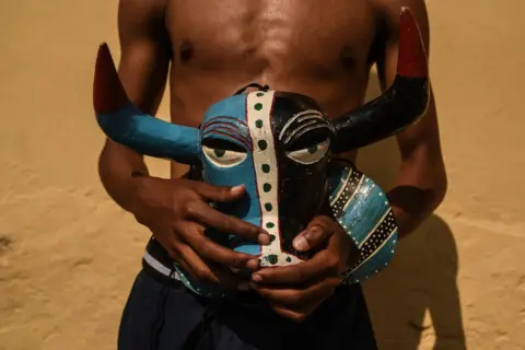 Hector Quintanar / Getty Images A man holds a brightly painted wooden mask carved to look like a bull's head.