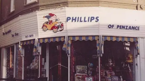 Roger Salter A toy shop on a corner in Penzance back in the 1980's with long windows and double front wooden door and a Noddy car sign visible above the front door. The words Phillips and 'specialist toy shop' are above the door.