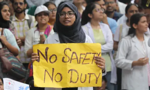 A woman holds up a sign saying "no safety, no duty"