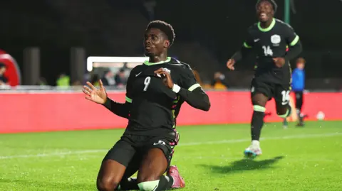 Mohamed Toure slides on his knees to celebrate a goal for Australia against New Zealand