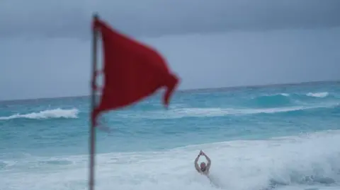 Reuters Un touriste se baigne sur une plage tandis qu'un drapeau rouge avertit les baigneurs des conditions dangereuses alors que la tempête tropicale Helene s'approche de la péninsule du Yucatan, à Cancun, au Mexique, le 24 septembre.