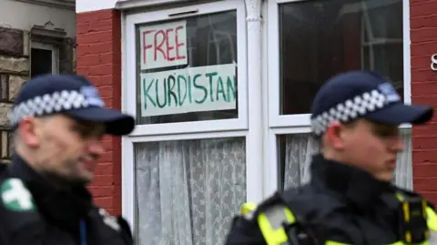 Reuters A "Free Kurdistan" sign is displayed in the window of a property as two police officers stand guard outside a Kurdish community centre in Haringey in London