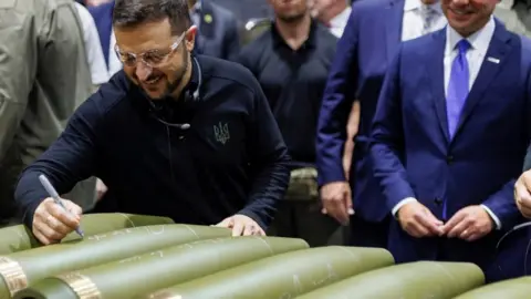 Ukrainian President Volodymyr Zelensky signs his name on a shell during a visit to a munitions plant