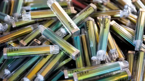 PA Media A close-up image of a pile of disposable vapes. All are the same shiny blue and gold colour.