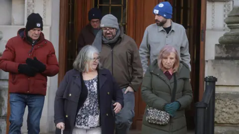 Pacemaker Members of Natalie McNally's family are pictured leaving the Royal Courts of Justice in Belfast. There are four men and three women. They are wearing coats and all four men have hats on. 