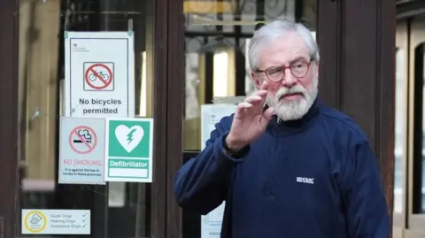 Gerry Adams raises his hand to wave at the High Court in London.