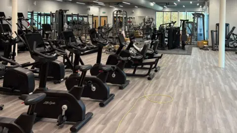 Rows of cardio machines in a gym. There are several cross fit machines and stationary bikes.