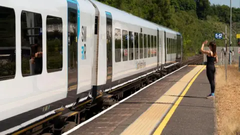 A woman waving from platform as a white South Western Railway passenger train departs Micheldever Station.