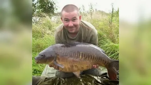 BBC Terry Ricketts, with short shaved hair, smiling into camera, wearing a green top and holding a large fish.