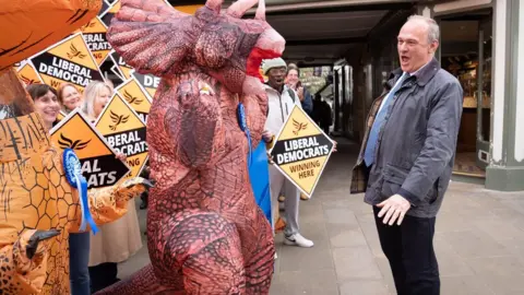 Liberal Democrats leader Sir Ed Davey with people in dinosaur costumes