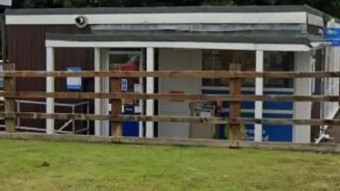 A single storey white building behind a brown fence.