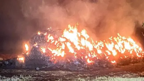 A fire service picture taken at night showing hay bales alight and smoke pouring into the sky