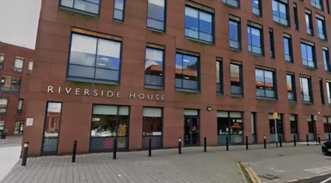 Google Maps A large red brick building with lots of big windows, and writing on the side saying 'Riverside House'