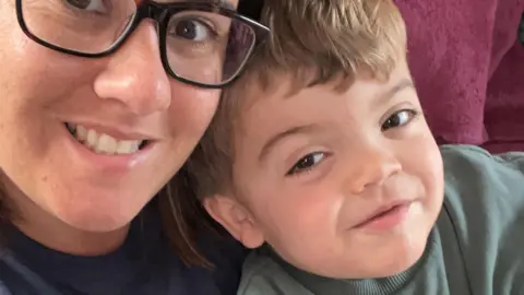 Holly and son Gunner smile at the camera. The picture shows their head and shoulders and Holly wears a blue jumper and Gunner has a green top. 