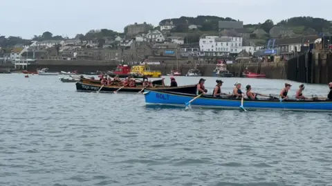 A side-on image of a crews sat in two gigs with oars out of the water as they race.