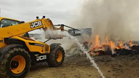 A yellow teleporter appears to be moving burning material while a jet of water is directed at the flames.
