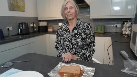 Dorothy standing in a kitchen with a tuna sandwich in foil on the work surface in front of her