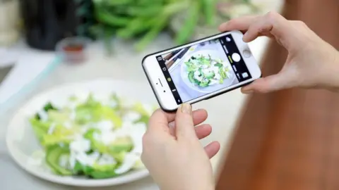 Getty Images Woman with an Iphone takes picture of an avocado salad