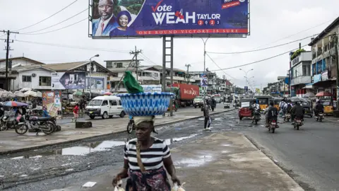 AFP A woman walks past a campaign billboard for the President of Liberia George Weah in Monrovia - 4 October 2023