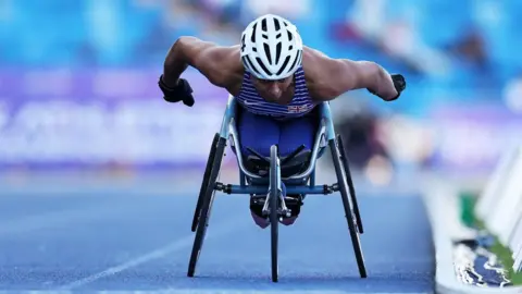 Getty Images An athlete wearing a blue and white t-shirt and blue leggings and white helmet in wheelchair race.