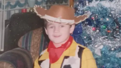 Family handout A photograph of Kaine as a child wearing a cowboy outfit and standing in front of a Christmas tree