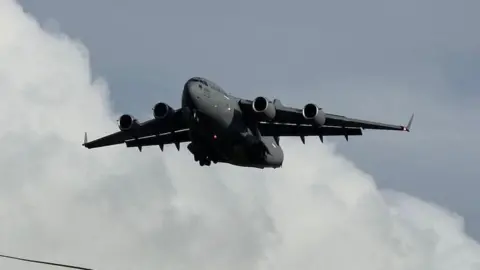  A large grey US Air Force military jet aircraft against a cloudy grey blue sky above a telegraph wire on Prestwick.