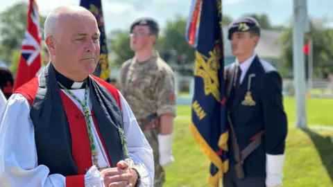 Archbishop of York Stephen Cottrell wearing a white, red and black robes and a dog collar, he has closely cropped grey hair.