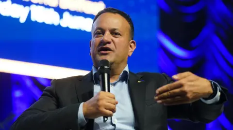 PA Man sitting in chair speaking on stage 