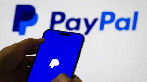 Getty Images PayPal's logo displayed on a smartphone, with a larger logo shown on a white background behind it.