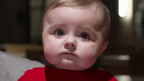 Ed Young/BBC A picture of six-month-old Daisy, wearing a red top, who stars in the video.