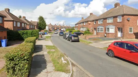 Street view image of Chesterfield Drive on a sunny day in 2023. It is a residential area with houses either side of the road and cars parked next to the pavement on the right hand side. 