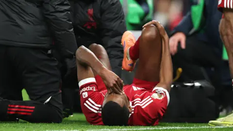 Alexander Isak lies on the pitch with his hand on his face holding his right leg