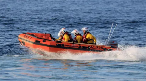Arangy at Sea, an orange lifeboat with four individuals wearing RNLI uniform inside. 