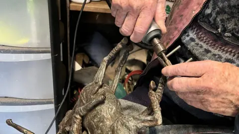 This is a close up image of Jan's hands as she uses a grinding tool to polish a horse sculpture.