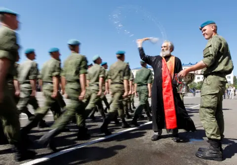 Eduard Korniyenko A priest sprays water as troops walk by