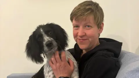 Supplied A woman and a dog looking down the lens of the camera. The woman is smiling and the dog is sat on her knee.