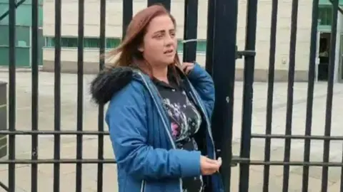 Jade Dempsey in mid-shot walking past security barrier outside Belfast Crown Court