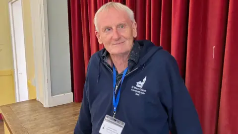 Shariqua Ahmed / BBC Roger wearing a blue jacket with St Mark's Church written on it 