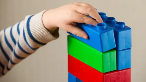Illustrative image of an anonymous young child playing with brightly coloured plastic blocks.