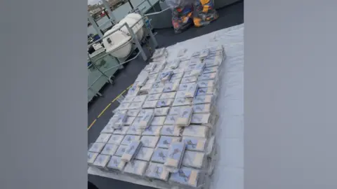 National Crime Agency a large pile of packages of a white substance lying on plastic sheeting on what appears to be the deck of a boat or ship