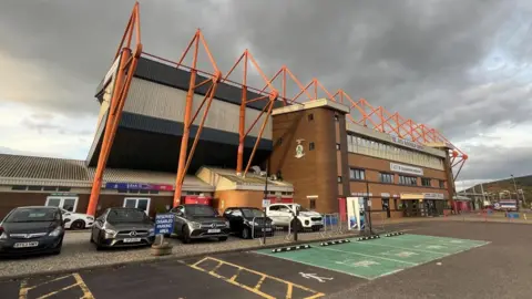 BBC ICT stadium and its car park. There are dark clouds above the football ground.