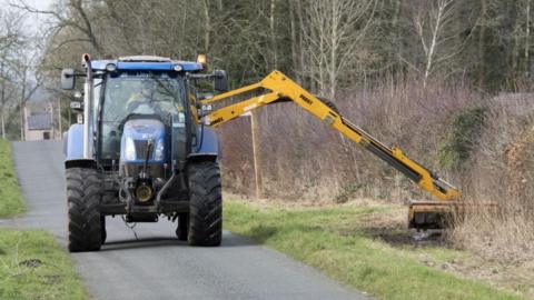 A tractor-mounted hedge cutter in action
